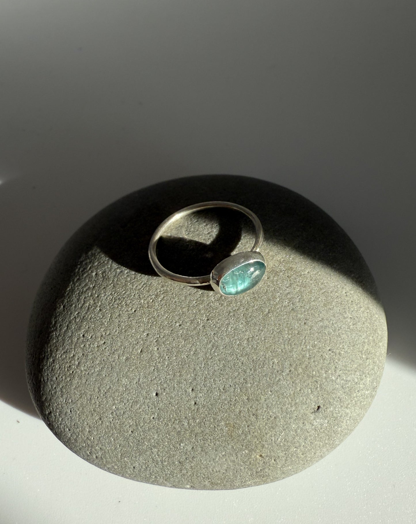 Silver ring with a green kyanite gemstone on a textured surface